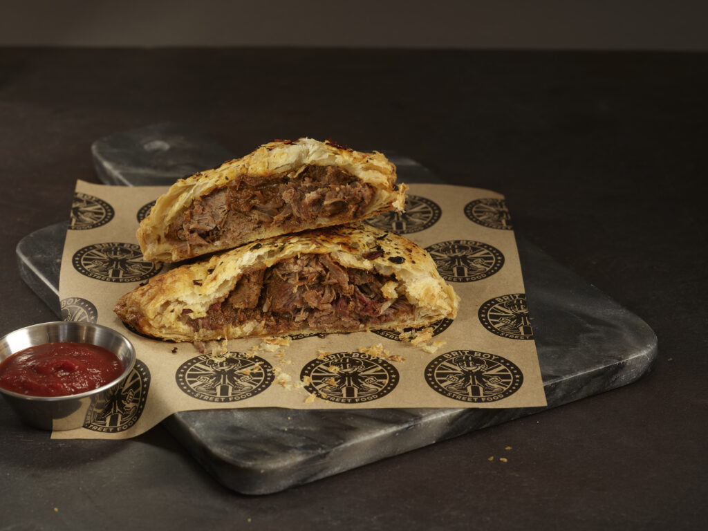 Brit Boy Birria Pasty Half with Lifestyle Background